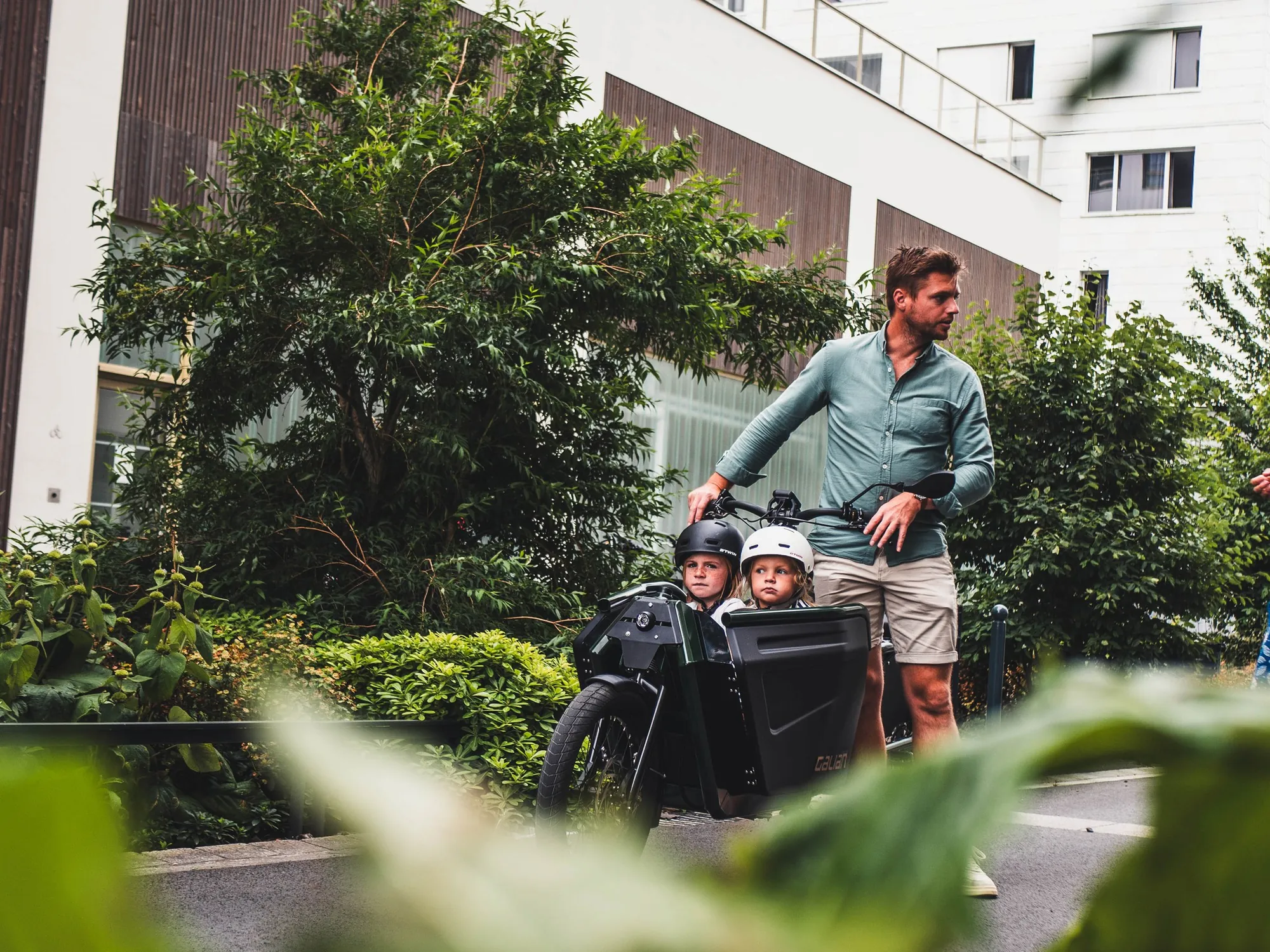 Un père et ses enfants sur un vélo cargo Galian, devant un immeuble